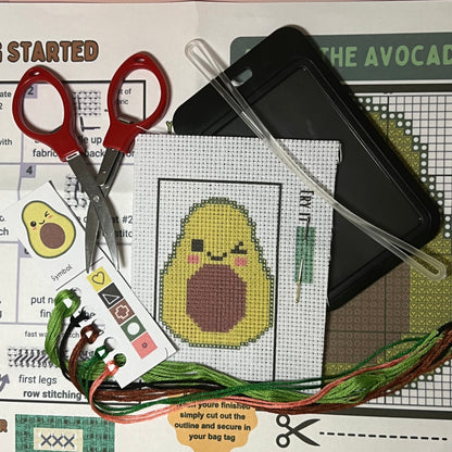 Avery the Avocado mini cross stitch DIY luggage tag kit with a black bag tag, luggage tag attachment, Scissors, needle and thread, stamped Aida fabric, color instructions