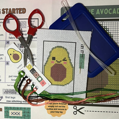 Avery the Avocado mini cross stitch DIY luggage tag kit with a dark blue bag tag, luggage tag attachment, Scissors, needle and thread, stamped Aida fabric, color instructions