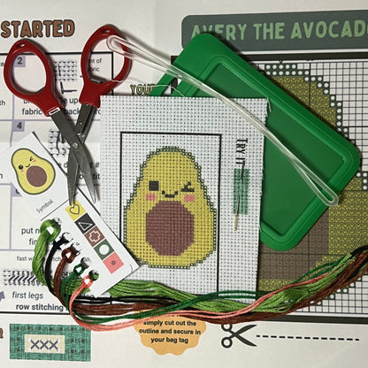 Avery the Avocado mini cross stitch DIY luggage tag kit with a green bag tag, luggage tag attachment, Scissors, needle and thread, stamped Aida fabric, color instructions