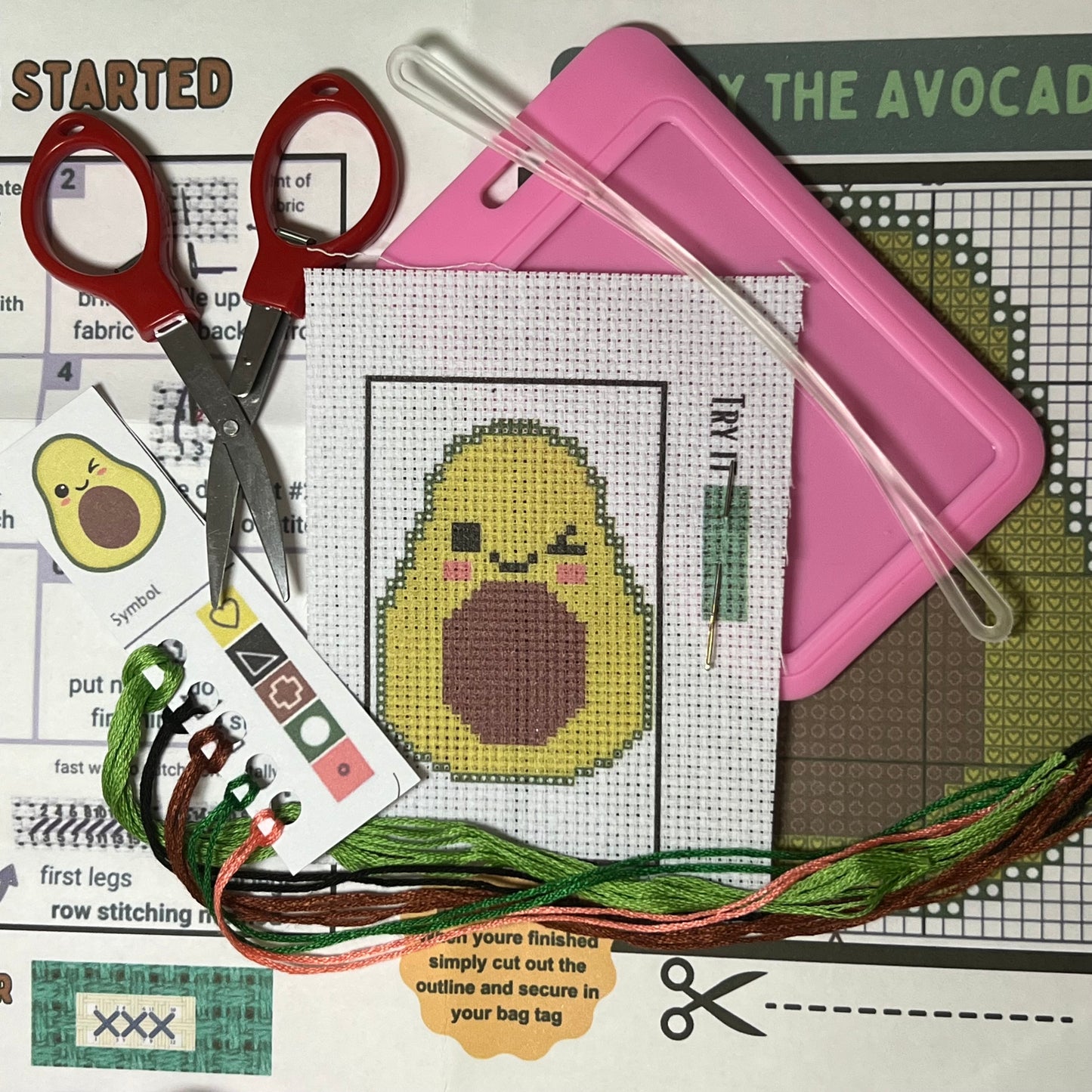 Avery the Avocado mini cross stitch DIY luggage tag kit with a pink bag tag, luggage tag attachment, Scissors, needle and thread, stamped Aida fabric, color instructions