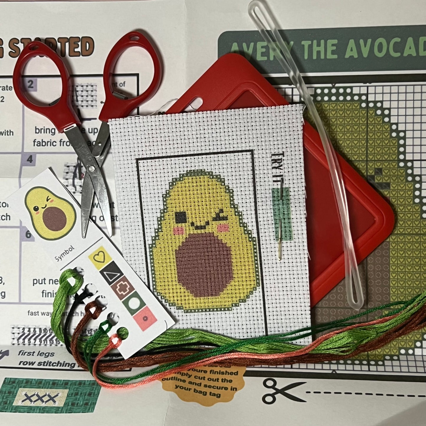 Avery the Avocado mini cross stitch DIY luggage tag kit with a red bag tag, luggage tag attachment, Scissors, needle and thread, stamped Aida fabric, color instructions