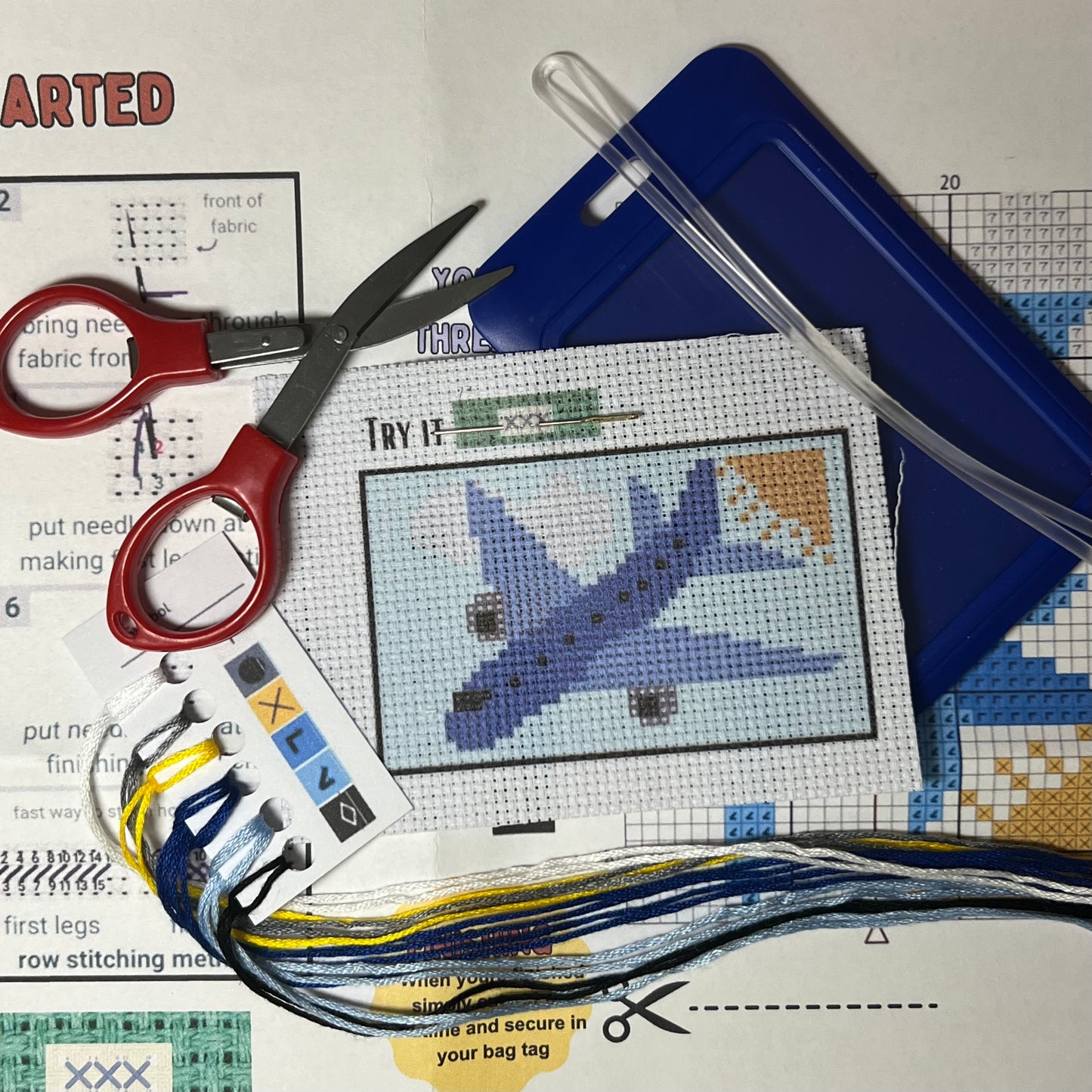 Blue Airplane in the Clouds mini cross stitch DIY luggage tag kit with a dark blue bag tag, luggage tag attachment, Scissors, needle and thread, stamped Aida fabric, color instructions