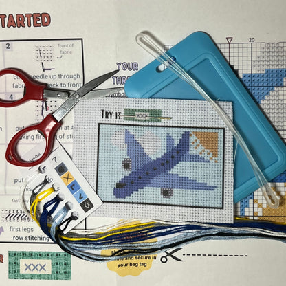 Blue Airplane in the Clouds mini cross stitch DIY luggage tag kit with a light blue bag tag, luggage tag attachment, Scissors, needle and thread, stamped Aida fabric, color instructions