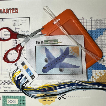 Blue Airplane in the Clouds mini cross stitch DIY luggage tag kit with a orange bag tag, luggage tag attachment, Scissors, needle and thread, stamped Aida fabric, color instructions