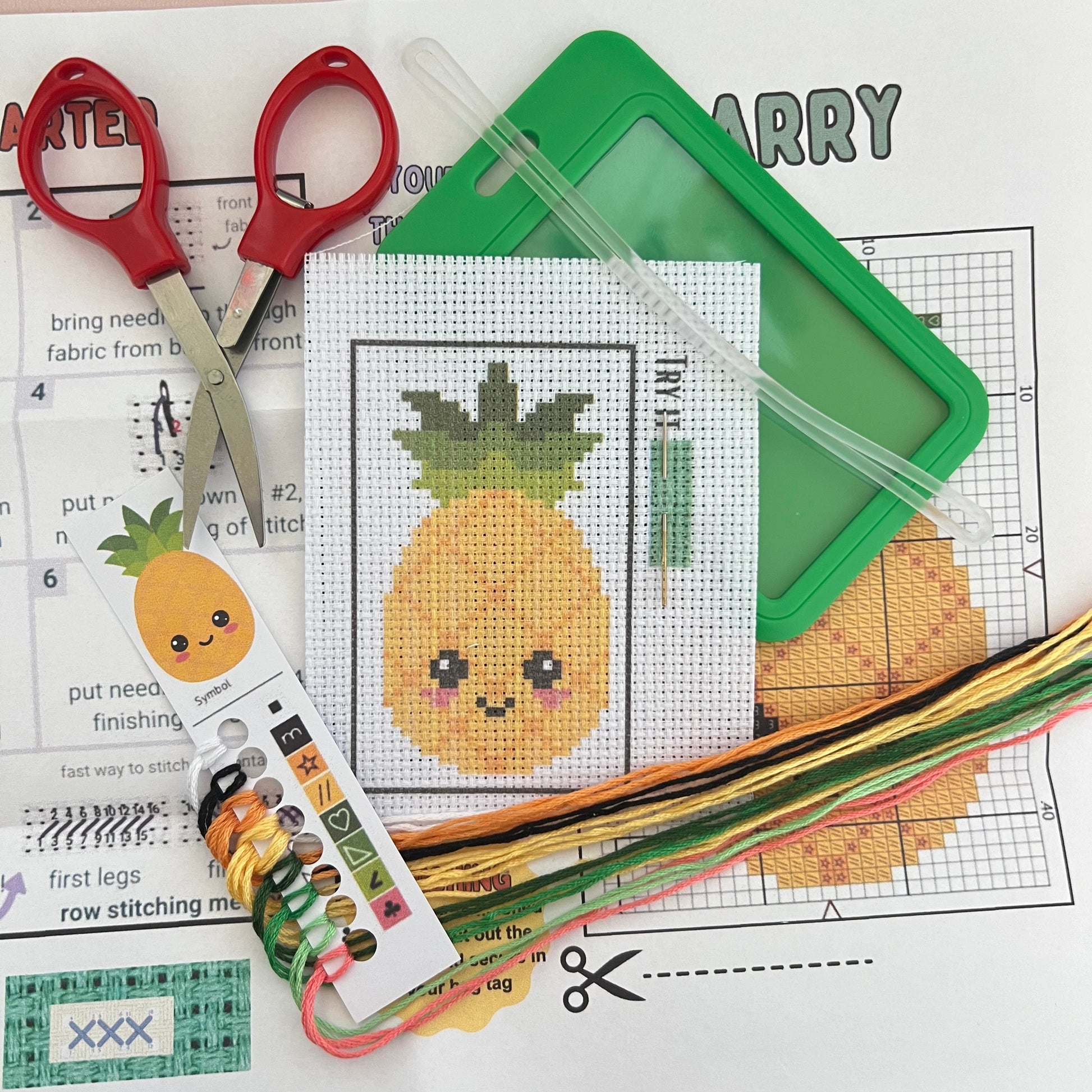 Larry the Pineapple mini cross stitch DIY luggage tag kit with a green bag tag, luggage tag attachment, Scissors, needle and thread, stamped Aida fabric, color instructions