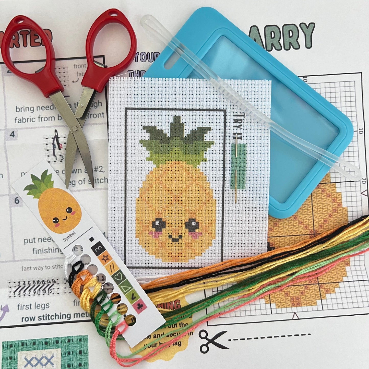 Larry the Pineapple mini cross stitch DIY luggage tag kit with a light blue bag tag, luggage tag attachment, Scissors, needle and thread, stamped Aida fabric, color instructions