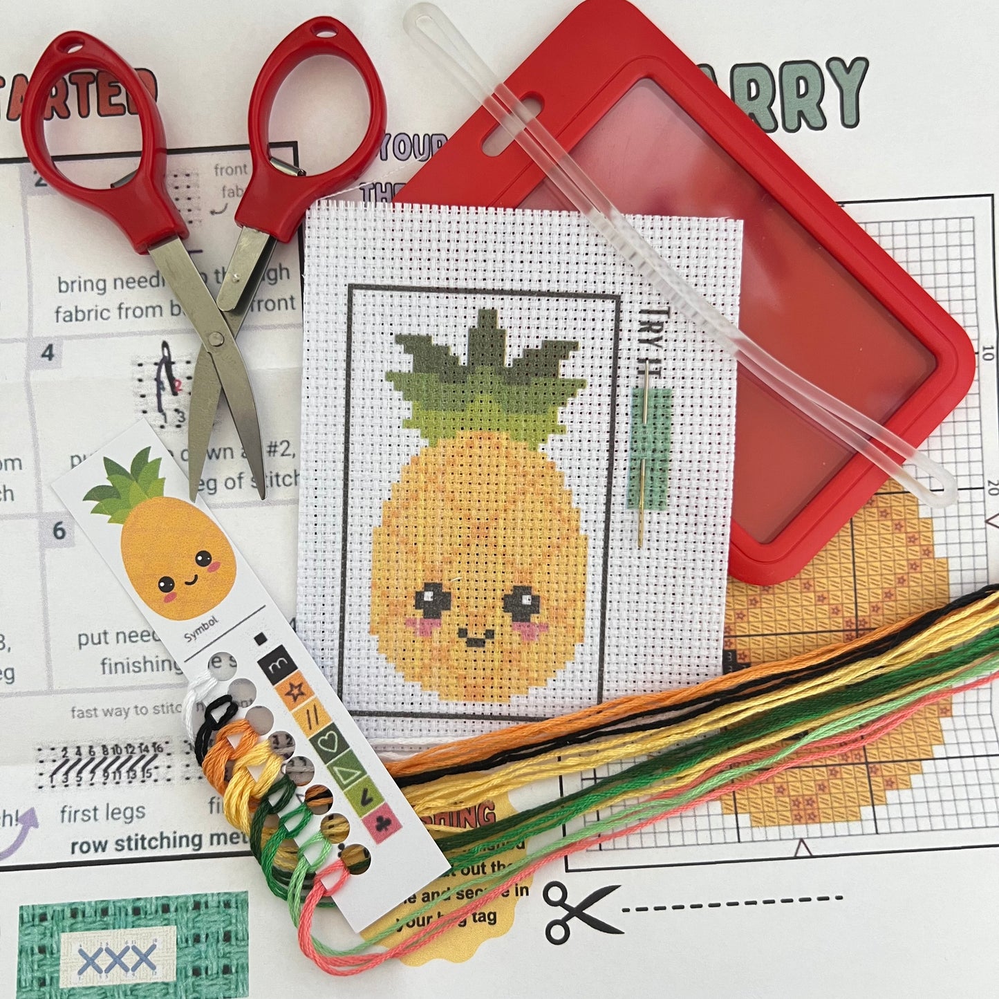 Larry the Pineapple mini cross stitch DIY luggage tag kit with a red bag tag, luggage tag attachment, Scissors, needle and thread, stamped Aida fabric, color instructions