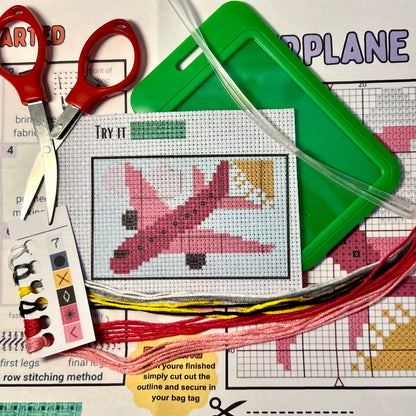 Pink Airplane cross stitch DIY luggage tag kit with a emerald green bag tag, luggage tag attachment, Scissors, needle and thread, stamped Aida fabric, color instructions